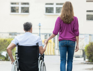 Une femme accompagne son marie en fauteuil roulant lors d'une sortie