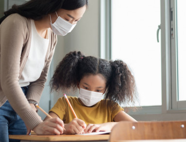 Une fillette et sa maîtresse portent un masque dans la classe.