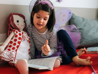 Une petite fille lit un livre à sa poupée.