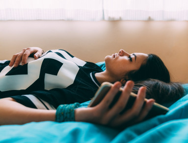 une jeune fille est allongée sur le dos sur son lit avec son portable dans les mains
