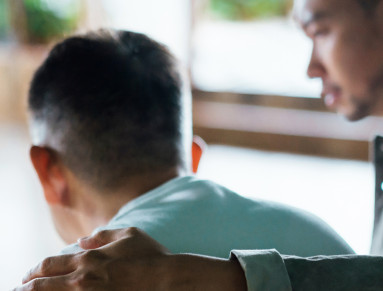 Un jeune homme pose son bras et sa main sur l'épaule d'un homme plus âgé