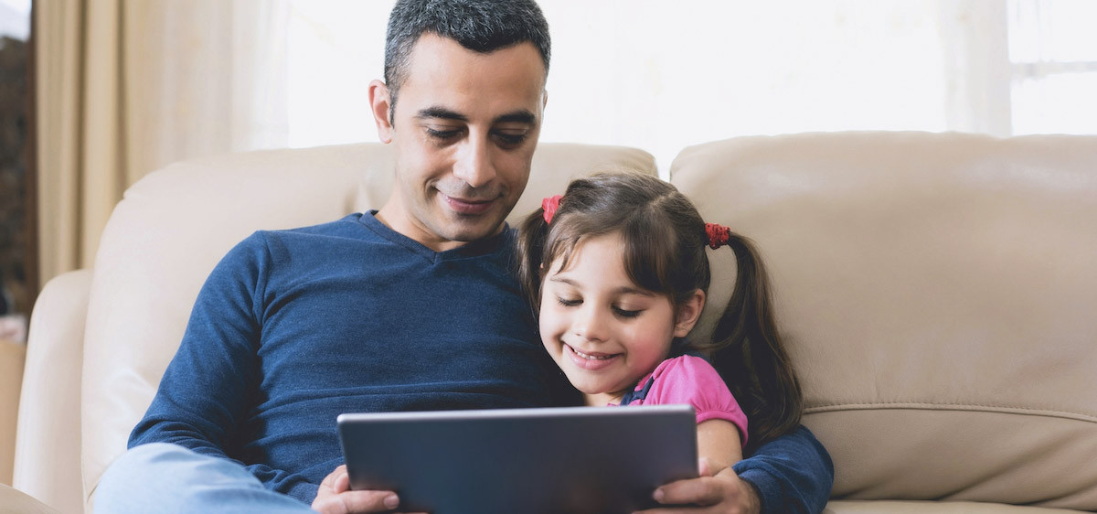 Un père lit une histoire à sa fille sur une tablette.