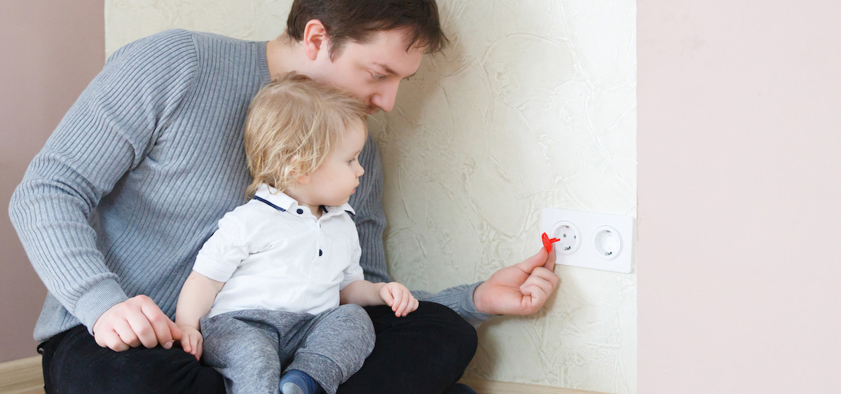 Un enfant touche une prise électrique protégée par un cache-prise.