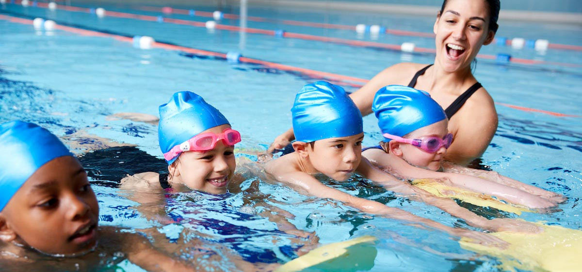 Quatre enfants suivent un cours de natation avec leur professeur.