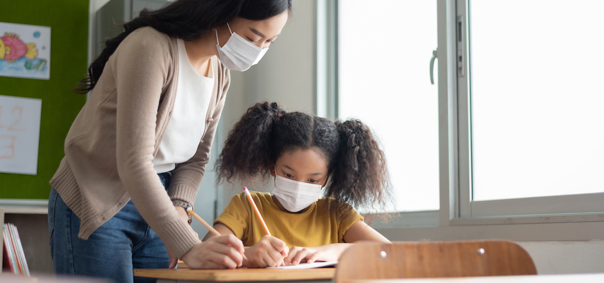 Une fillette et sa maîtresse portent un masque dans la classe.
