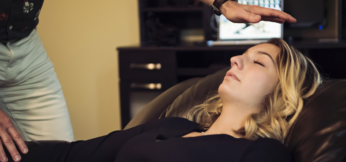 Une femme, yeux fermés, allongée sur le dos, est hypnosée par un médecin